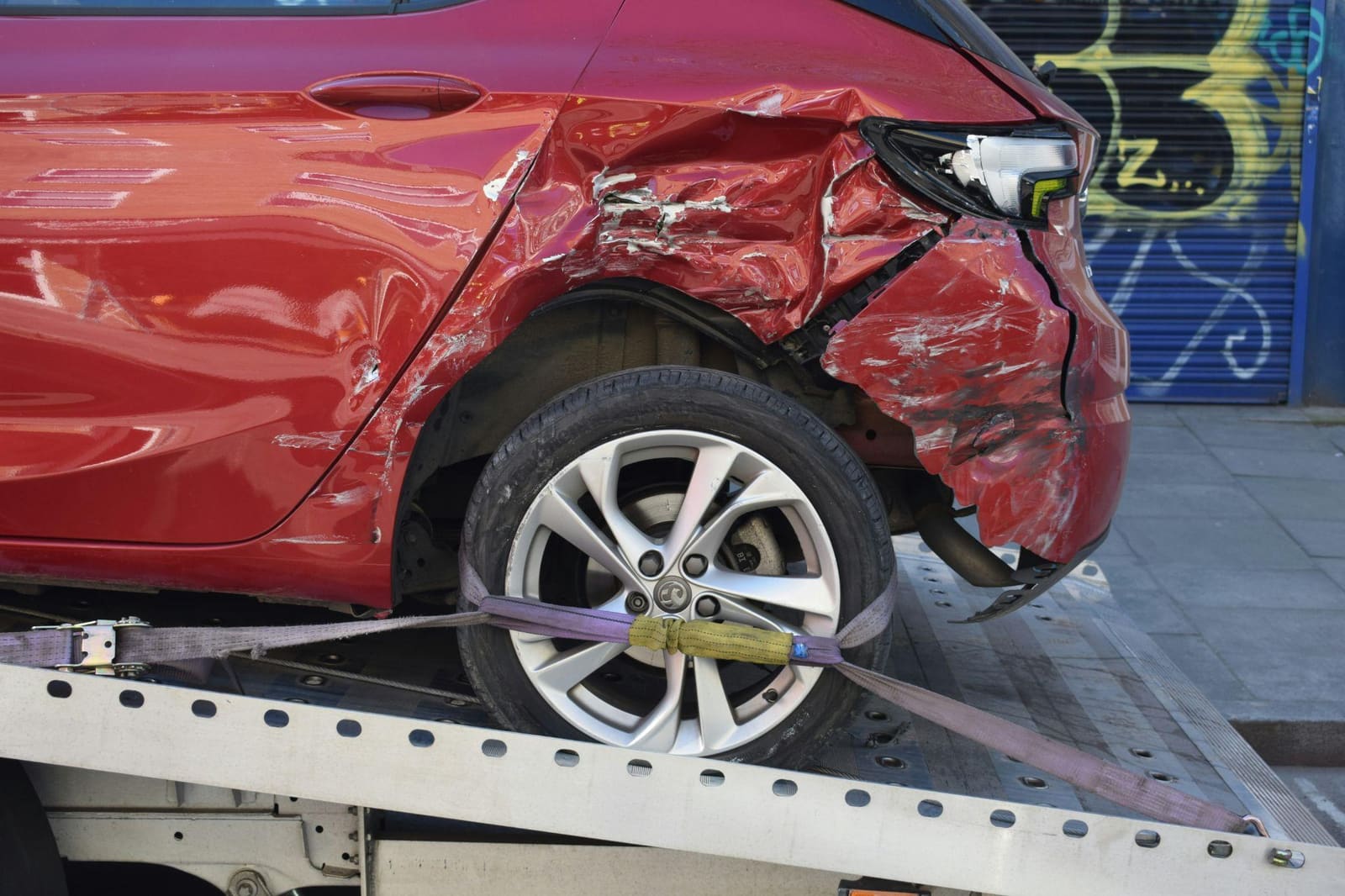 Red hatchback with severe rear-end collision damage loaded onto a flatbed recovery truck