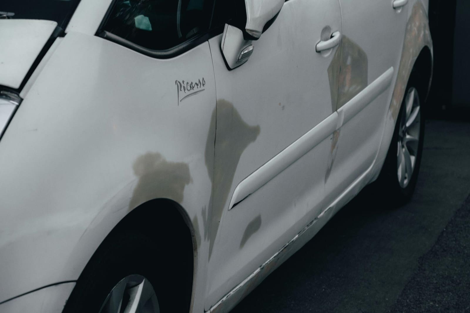 Scuffed and scratched paintwork along the front wing and door of a white Citroën C4 Picasso